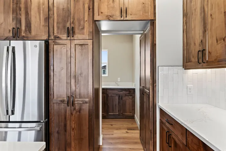 Kitchen featuring rich wood cabinetry, stainless steel refrigerator, white subway tile backsplash, and light-toned countertops