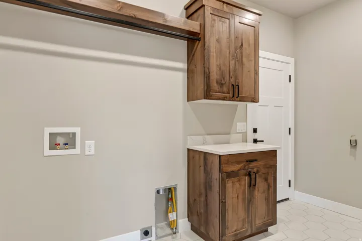 Laundry area with wood-finish cabinetry, light-toned countertop, and hexagonal floor tiling