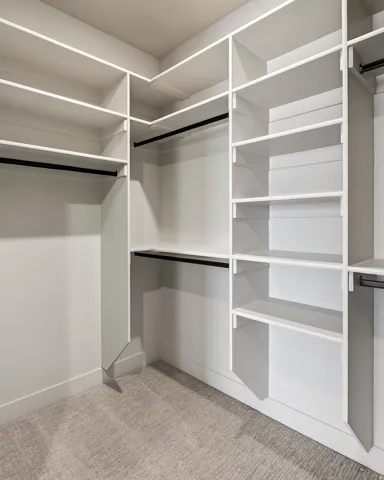 Walk-in closet featuring built-in white shelving, multiple hanging rods, and light-toned carpet flooring