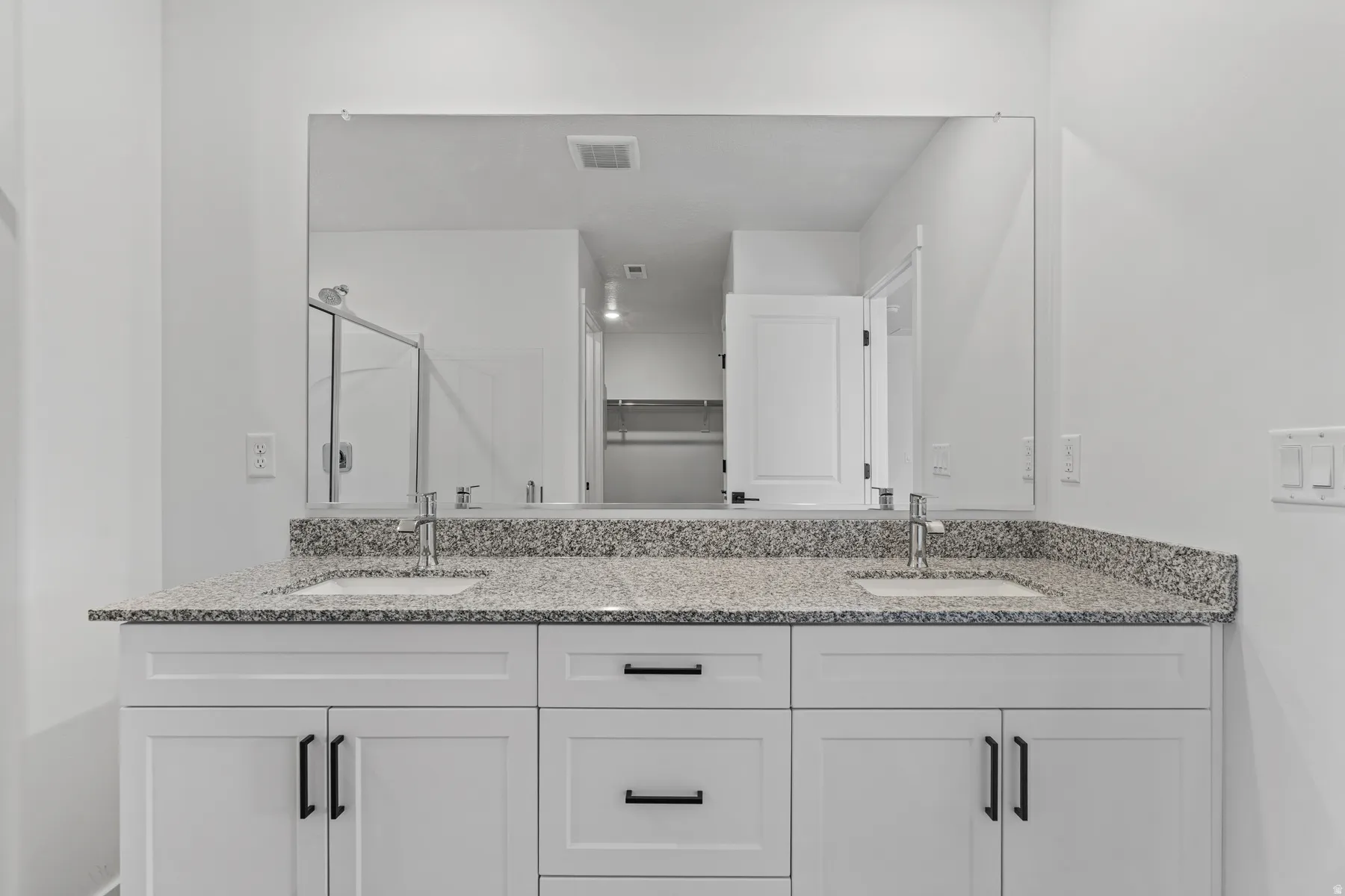 Dual vanity featuring white shaker cabinetry, black hardware, integrated sinks, and a speckled countertop