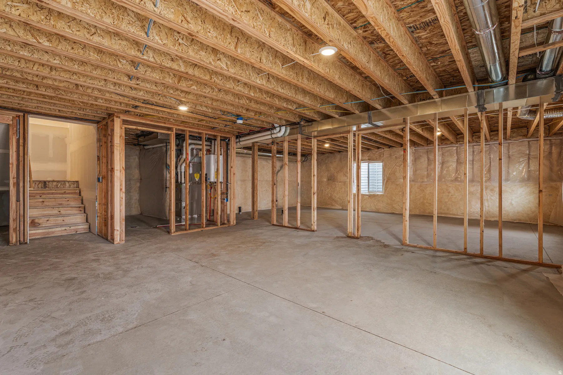 Unfinished lower level with exposed wood joists and subflooring, concrete slab flooring, and framed interior walls