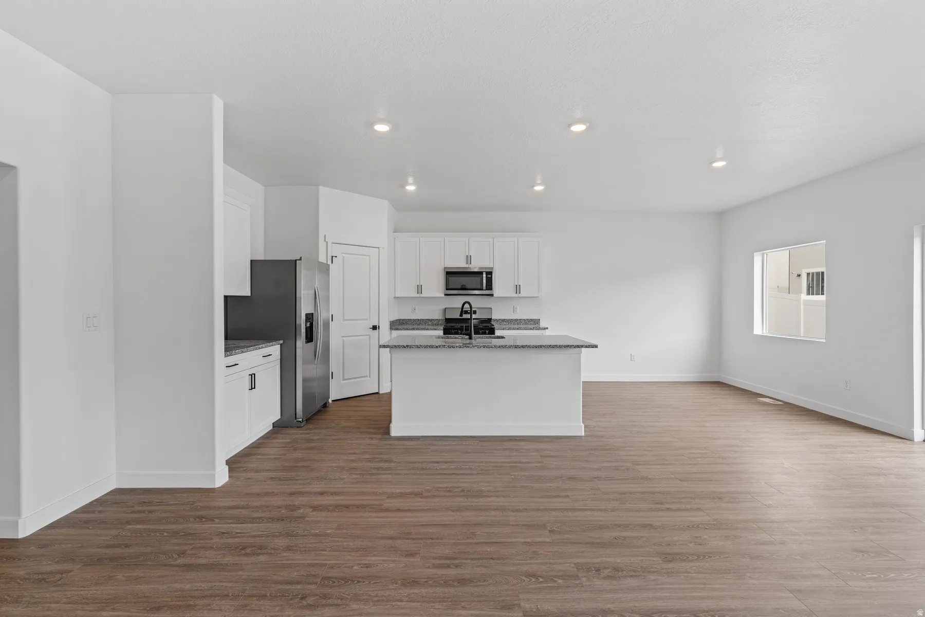 Open-concept living area featuring wood-finish flooring throughout, a kitchen island with stone countertops, white cabinetry, and recessed lighting