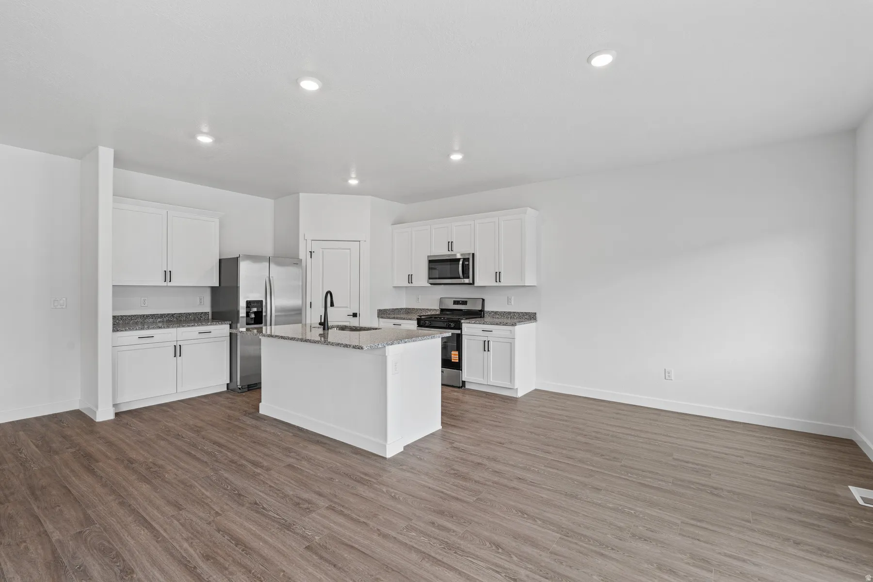 Modern kitchen featuring white cabinetry, stainless steel appliances, a center island with sink, granite countertops, and wood-finish flooring