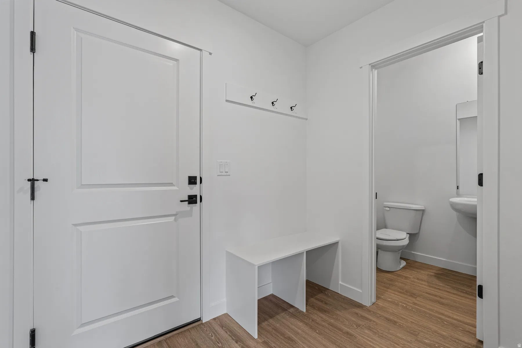 Entryway featuring a white paneled door with matte black hardware, wood-finish flooring, a built-in bench, and a wall-mounted coat rack