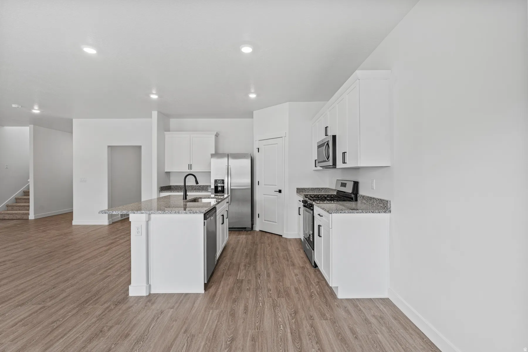 Bright kitchen featuring white cabinetry, a central island with a sink, stainless steel appliances, granite-style countertops, and wood-finish flooring