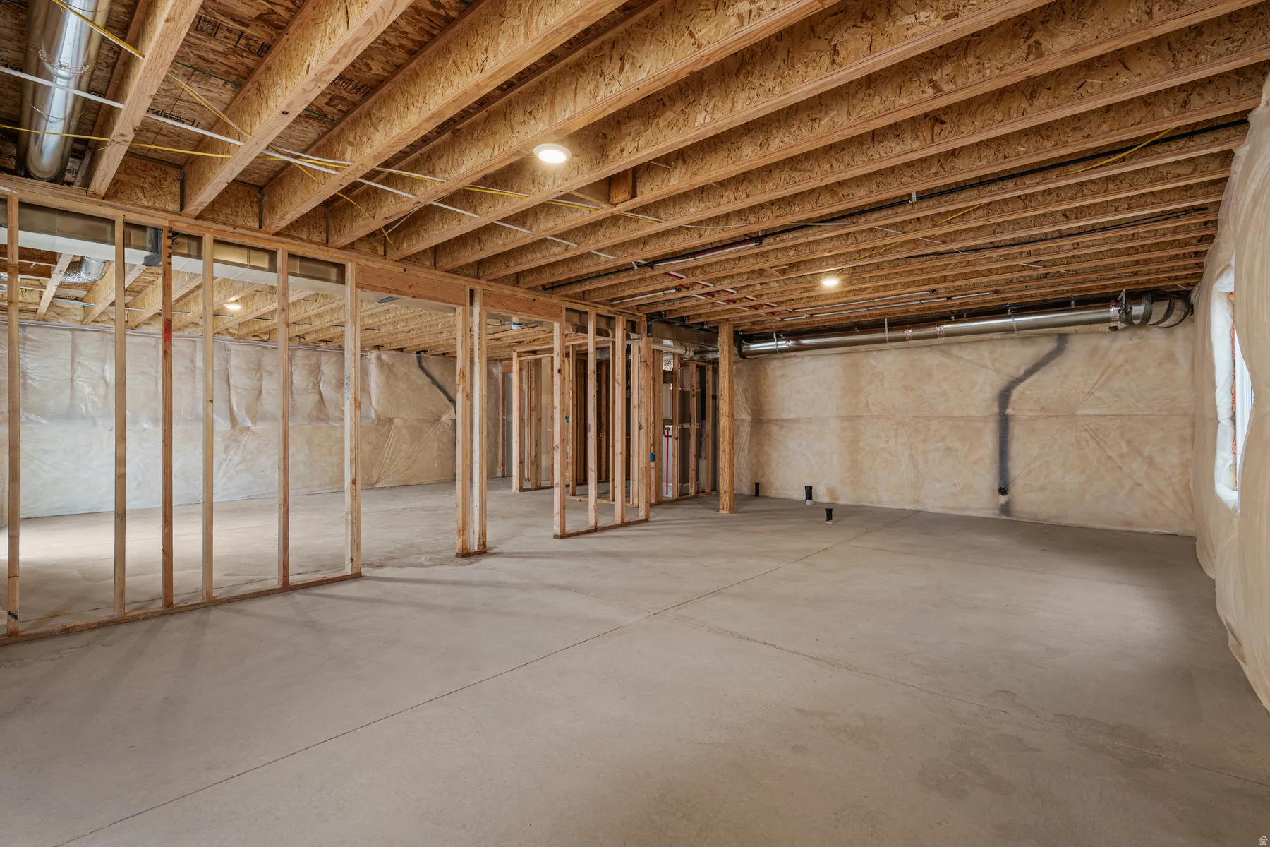 Unfinished basement featuring exposed wood joists, concrete flooring, and partial framing