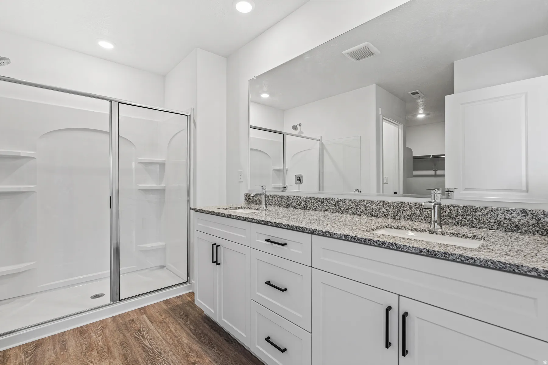Modern bathroom featuring a dual vanity with white cabinetry, matte black hardware, and speckled stone countertops