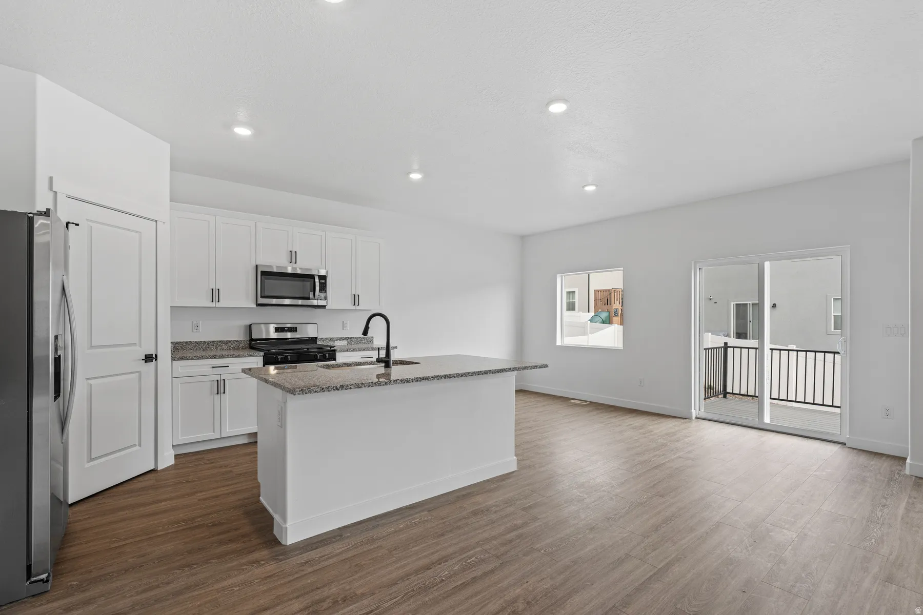 Open-concept living area featuring wood-finish flooring, recessed lighting, and a kitchen island with stone countertops