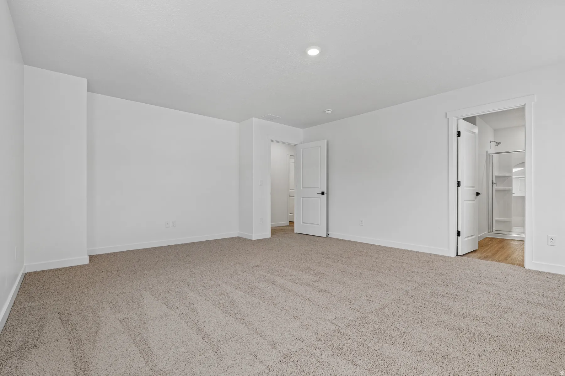 Spacious interior room featuring light-toned carpeting, white walls, and recessed lighting