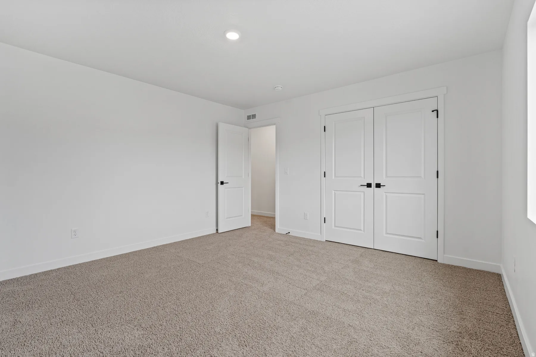 Carpeted room featuring white walls, a single recessed light fixture, two white paneled doors with black hardware, and a white baseboard trim