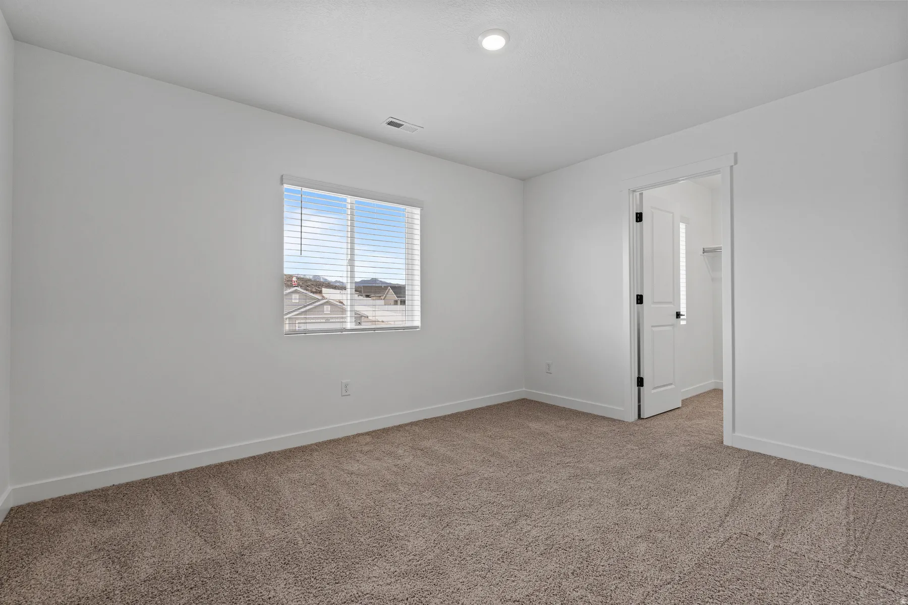 Carpeted room with white walls, a single window featuring horizontal blinds, and a recessed ceiling light
