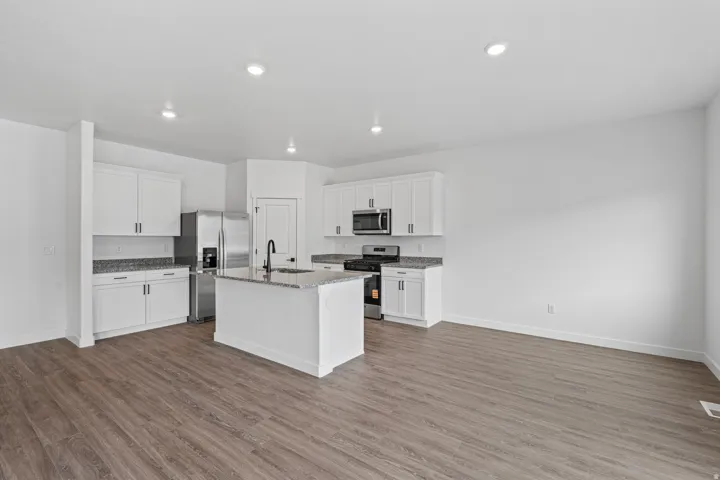 Modern kitchen featuring white cabinetry, stainless steel appliances, a center island with sink, granite countertops, and wood-finish flooring