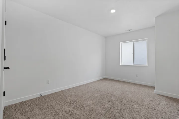 Spacious room featuring neutral carpeting, a large window, white walls, recessed lighting, and white baseboards