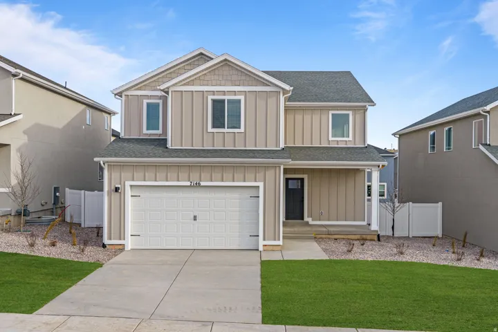 Contemporary two-story residence with a tan and gray exterior, featuring a covered front porch, an attached two-car garage, and a concrete driveway