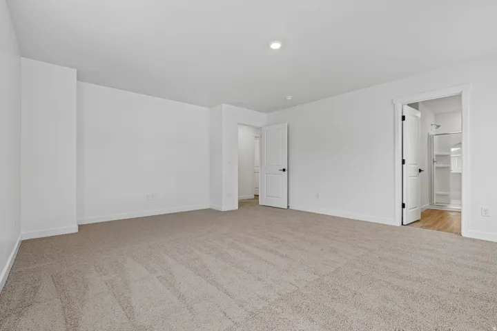 Spacious interior room featuring light-toned carpeting, white walls, and recessed lighting