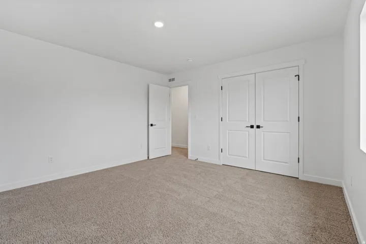 Carpeted room featuring white walls, a single recessed light fixture, two white paneled doors with black hardware, and a white baseboard trim