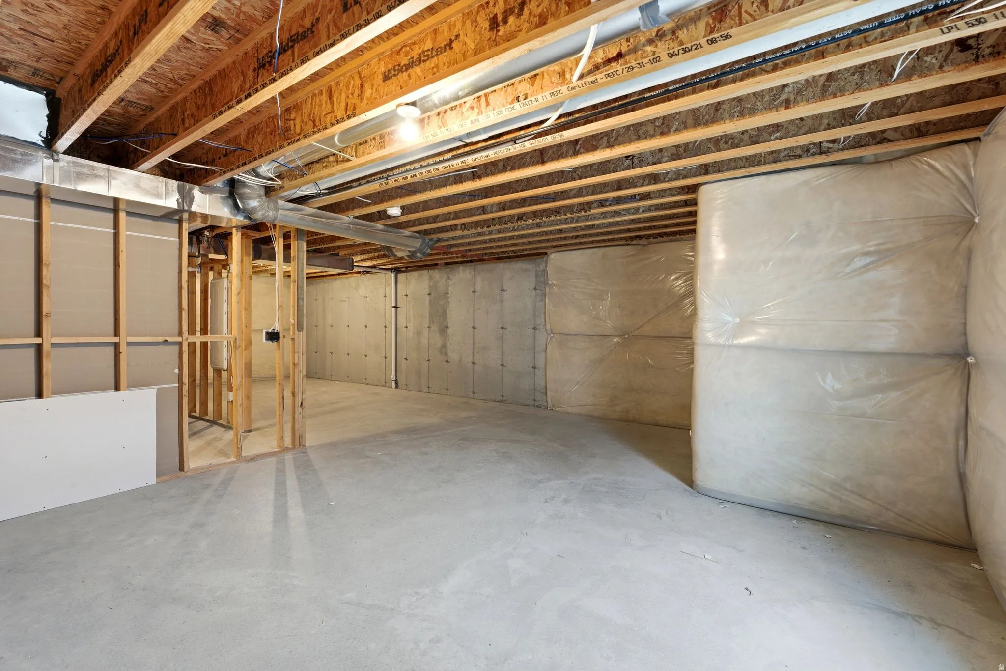 Unfinished basement with concrete flooring, exposed wood ceiling joists, and partial framing for future expansion