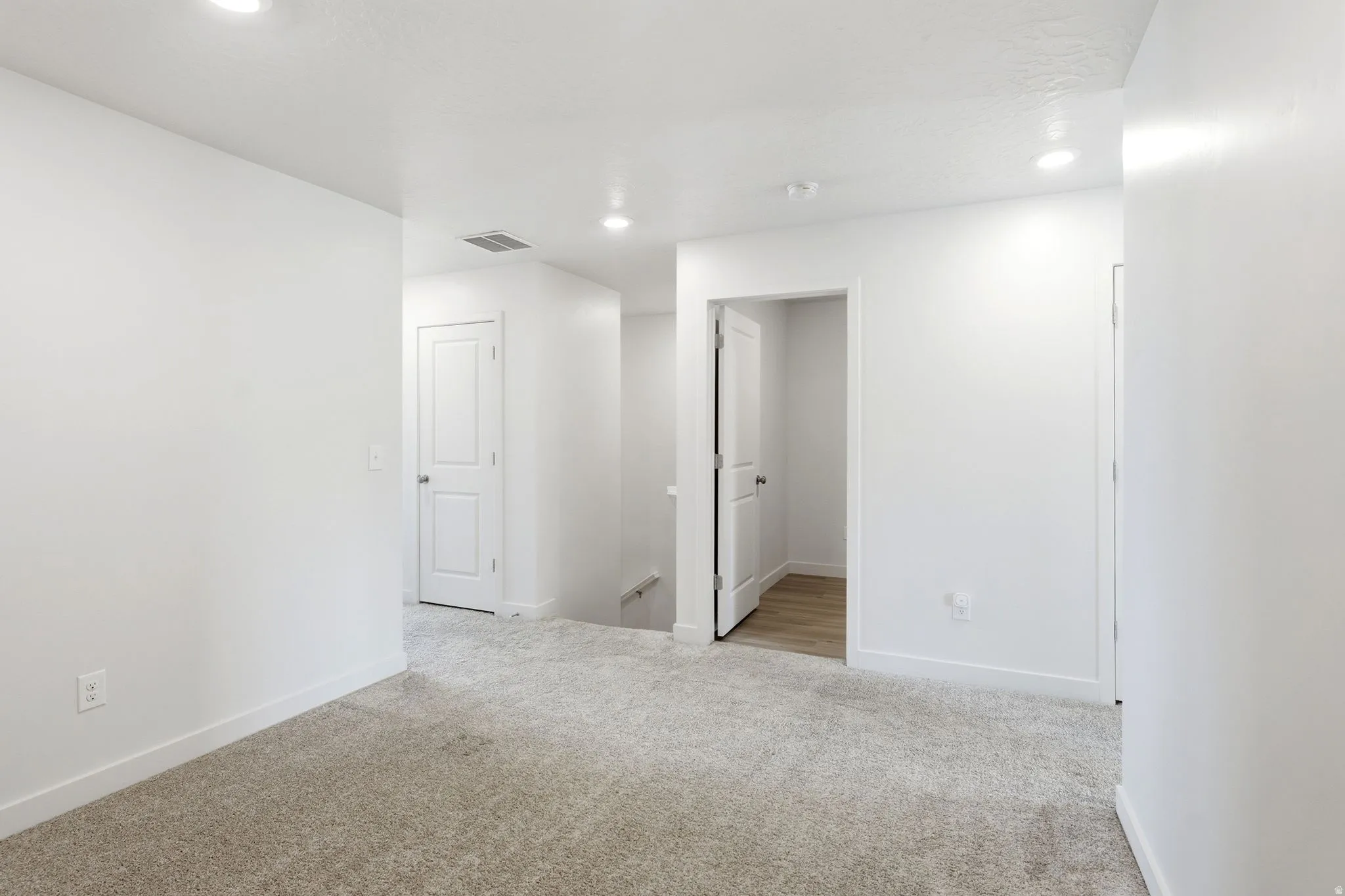 Carpeted hallway featuring bright white walls, recessed lighting, and white baseboards