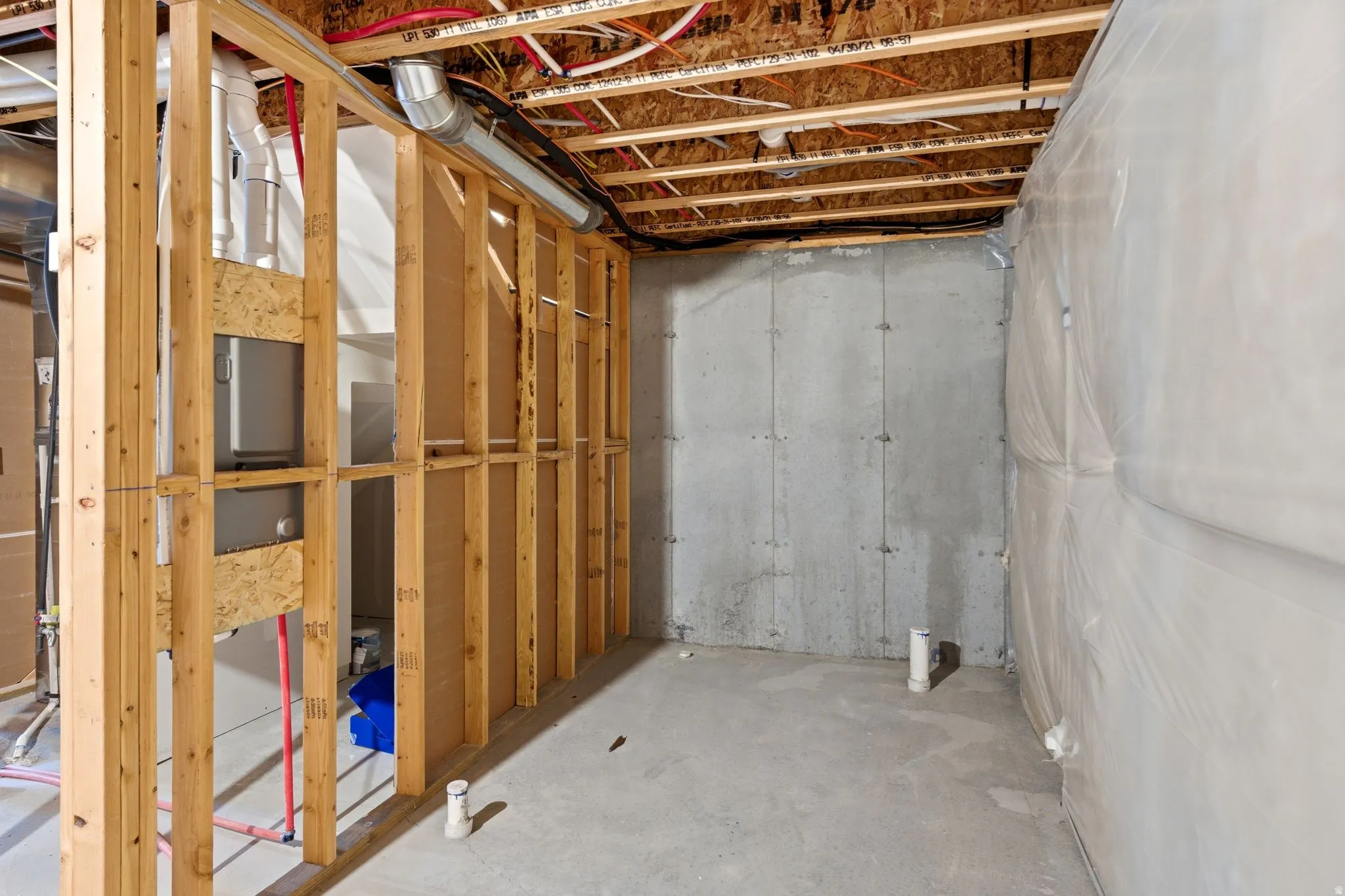 Unfinished basement featuring exposed wood framing, concrete foundation walls, and visible piping