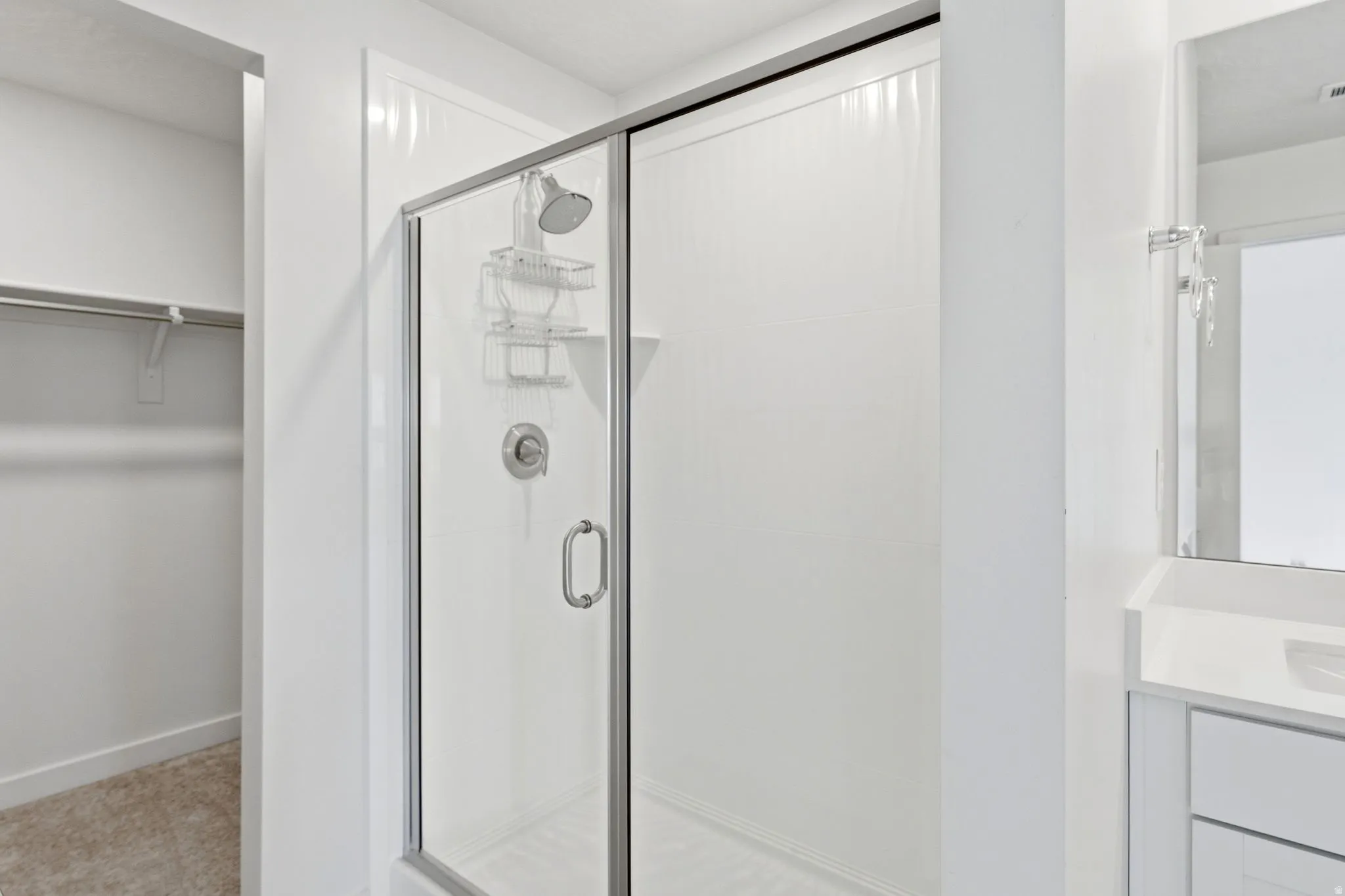 Walk-in shower with clear glass enclosure and chrome hardware, featuring a white shower surround, handheld showerhead, and built-in shelving