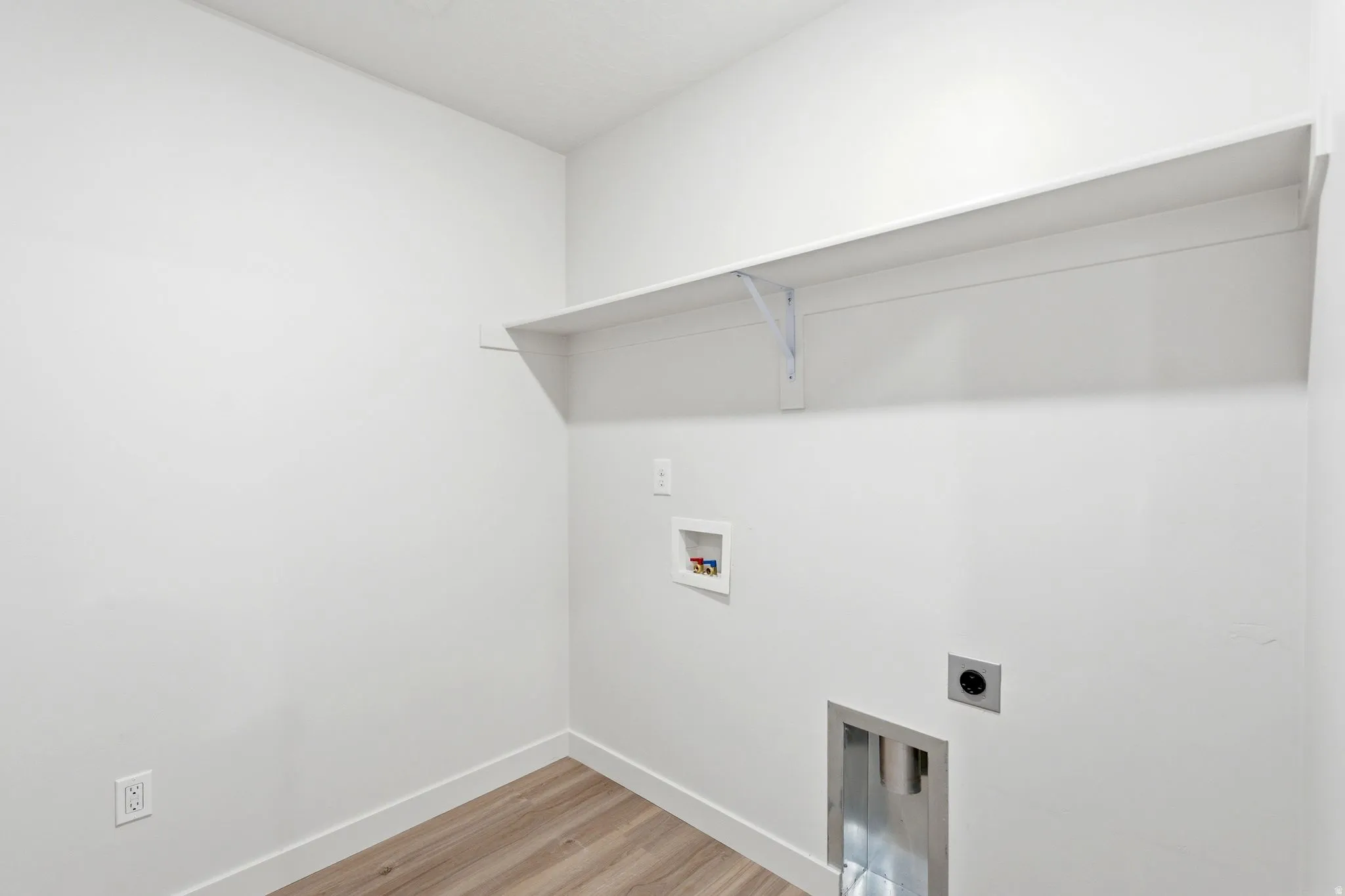 Utility room featuring a built-in shelf, wood-finish flooring, white baseboards, and bright white walls