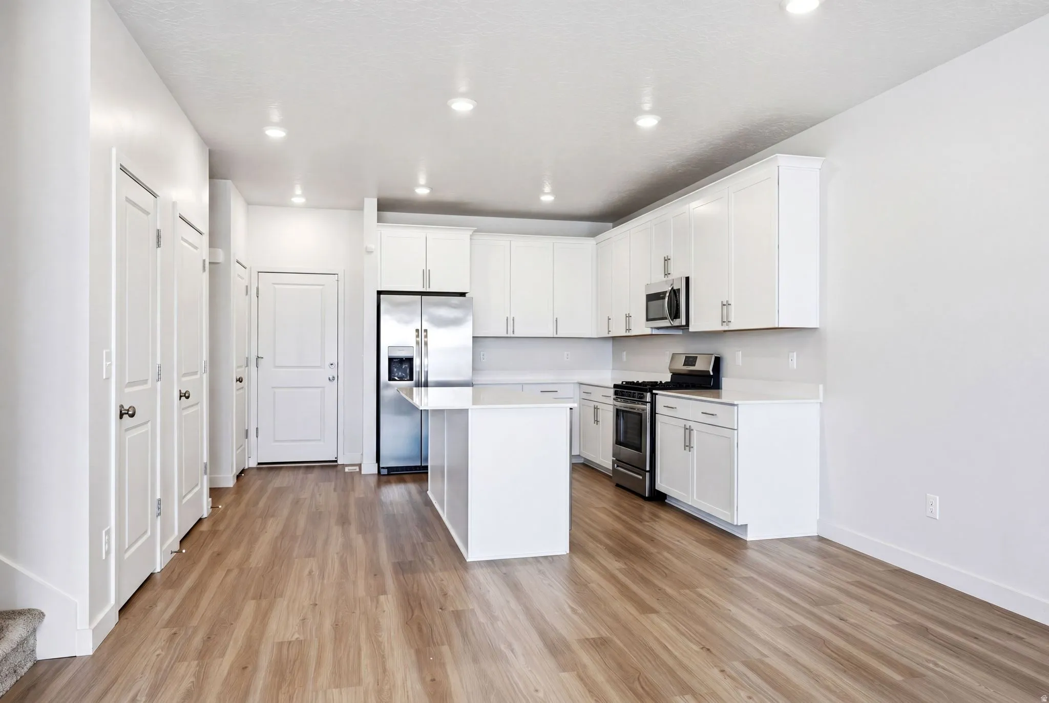 Modern kitchen featuring white cabinetry, a central island, stainless steel appliances, recessed lighting, and wood-finish flooring