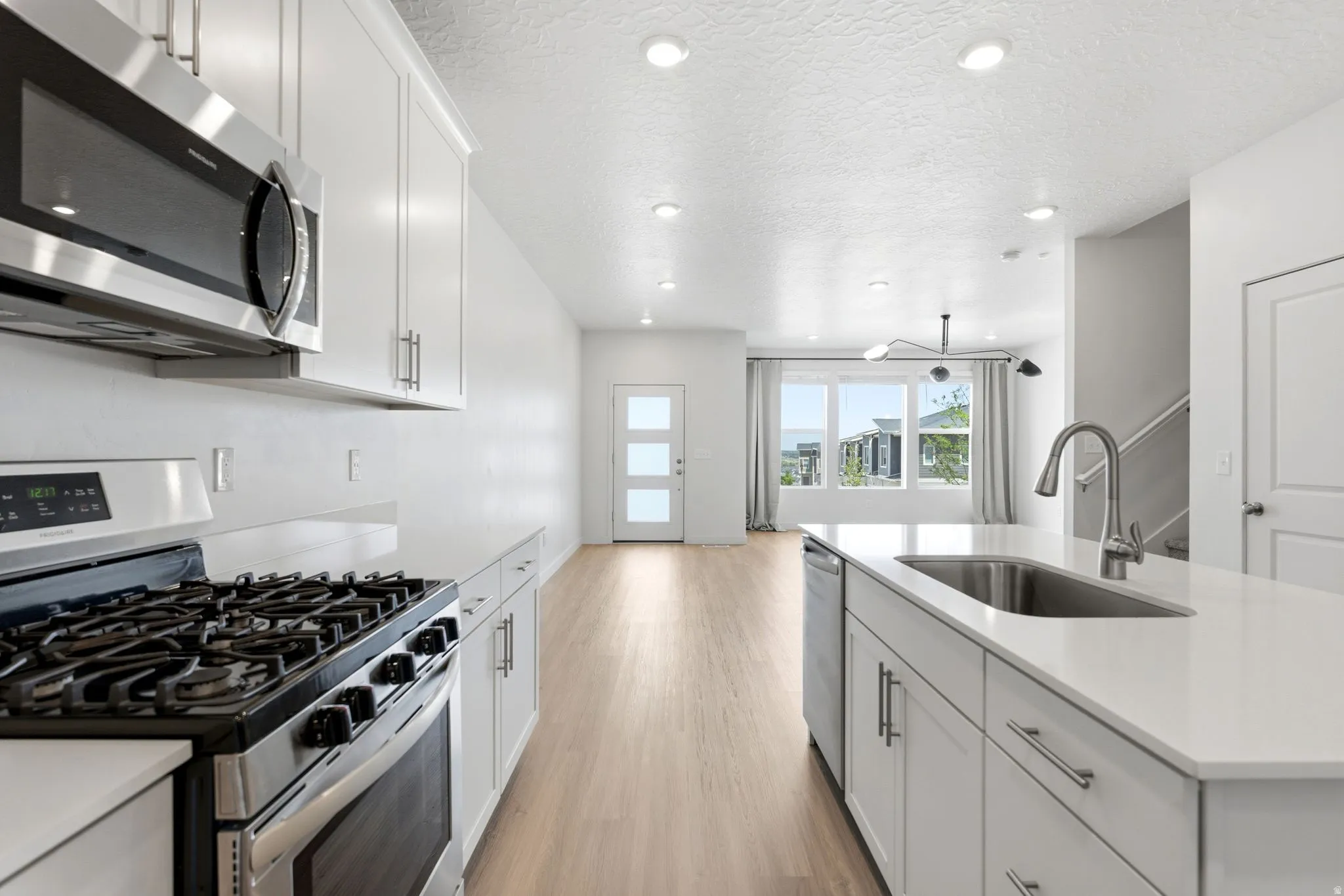 Modern kitchen featuring white cabinetry, stainless steel appliances, and light wood-finish flooring