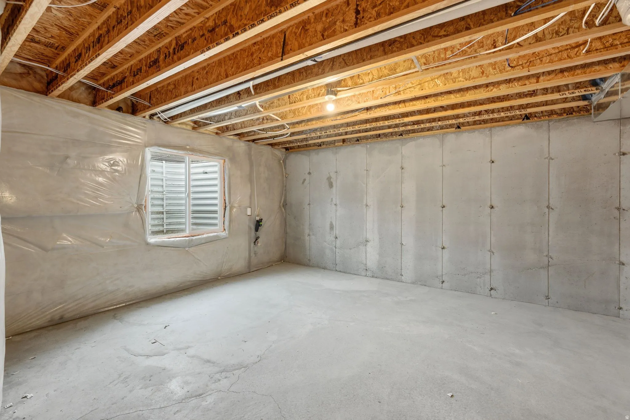 Unfinished basement with exposed wood joists, a concrete floor, and concrete walls