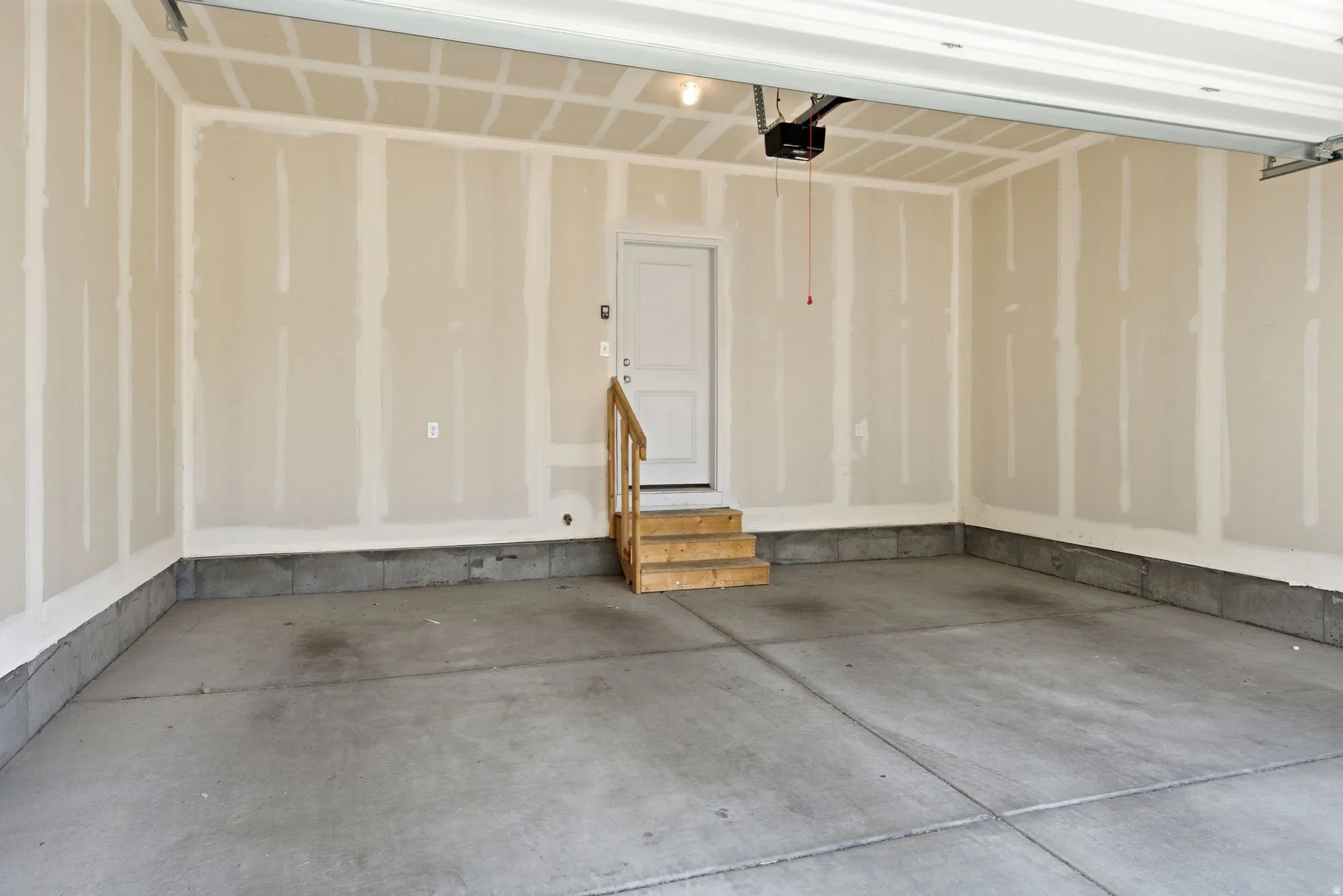 Concrete flooring garage with an interior access door, wooden steps, and a built-in garage door opener