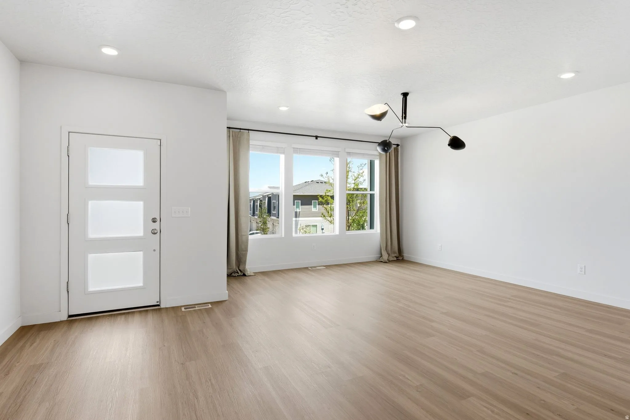 Open-concept living space with light wood-finish flooring, a contemporary multi-arm ceiling light fixture, and recessed lighting