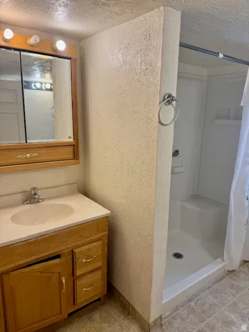 Bathroom featuring a light wood-finish vanity with an integrated sink, a mirrored medicine cabinet with integrated lighting, and a white shower stall with a grab bar