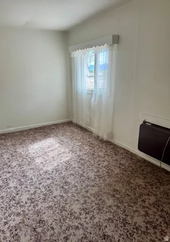 Room featuring patterned carpet flooring, a window with sheer curtains, and a wall-mounted heating unit