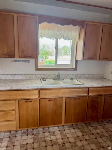 Kitchen featuring a double basin sink, ample wood cabinetry, patterned flooring, and a window providing natural light