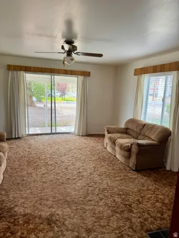 Spacious room featuring broadloom carpeting, a ceiling fan with integrated lighting, and multiple windows