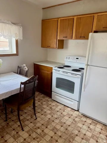 Kitchen featuring light wood cabinetry, white appliances, patterned floor tile, and a single window