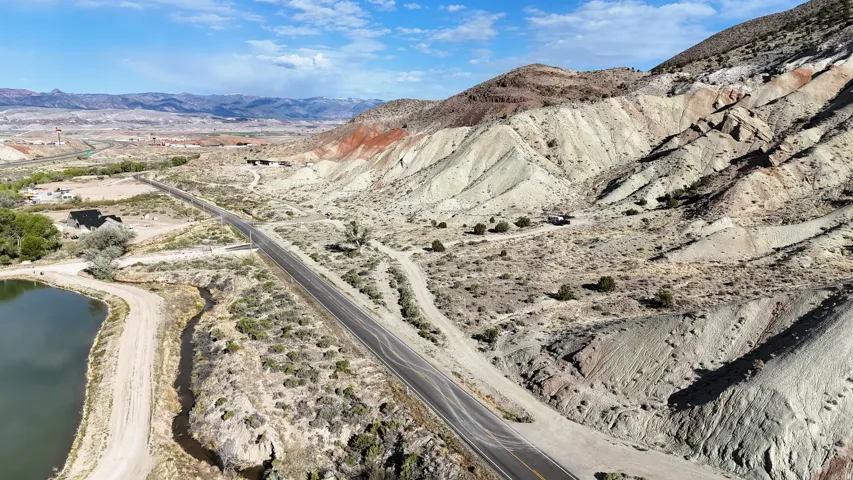 Expansive rural landscape featuring a private pond, paved road access, and distinct multi-colored geological formations