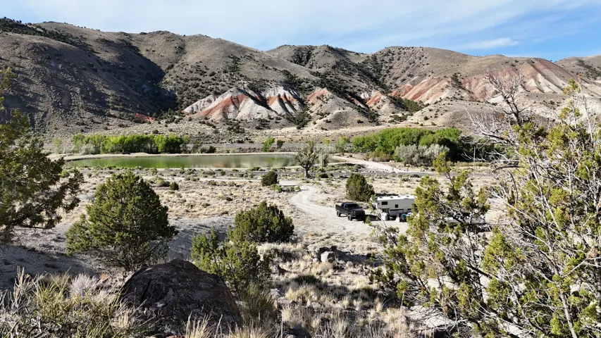 Mountainous landscape featuring a body of water, scattered evergreen bushes, and diverse geological formations