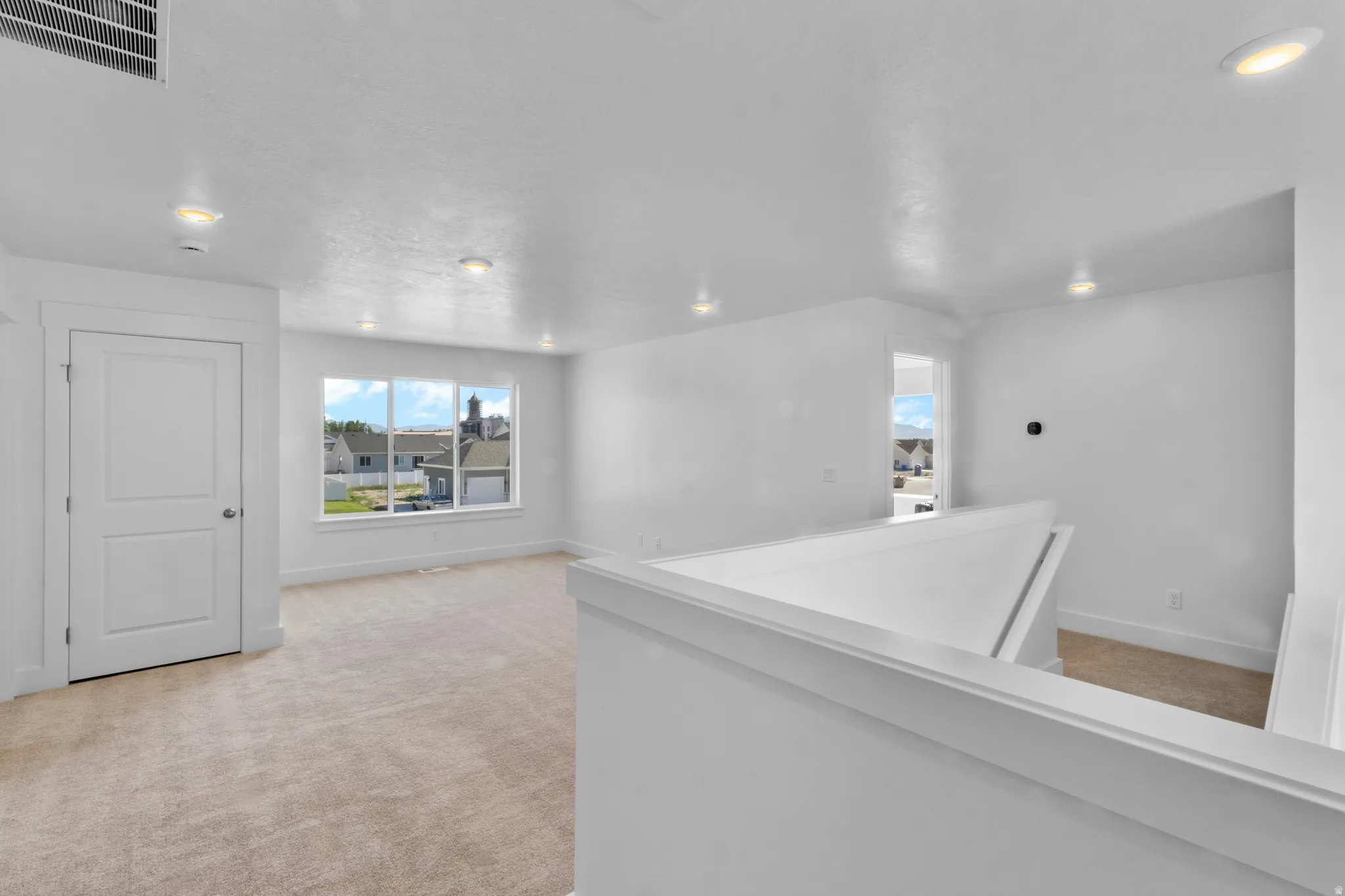 Bright upper-level area featuring a large window, recessed lighting, neutral carpeting, and white trim