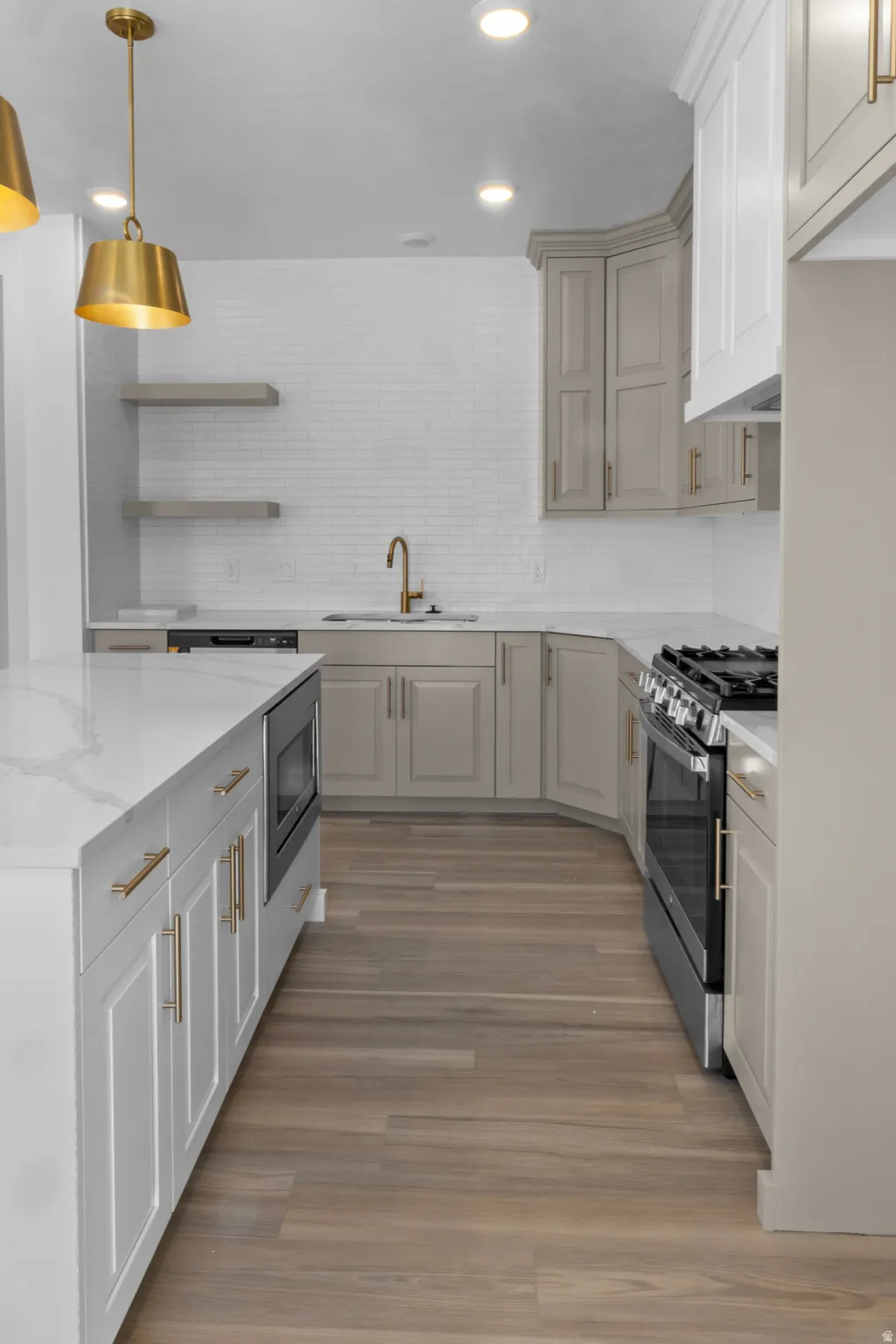 Modern kitchen featuring a large island with white cabinetry and integrated microwave, wood-finish flooring, a white subway tile backsplash, and two-tone cabinetry with gold hardware