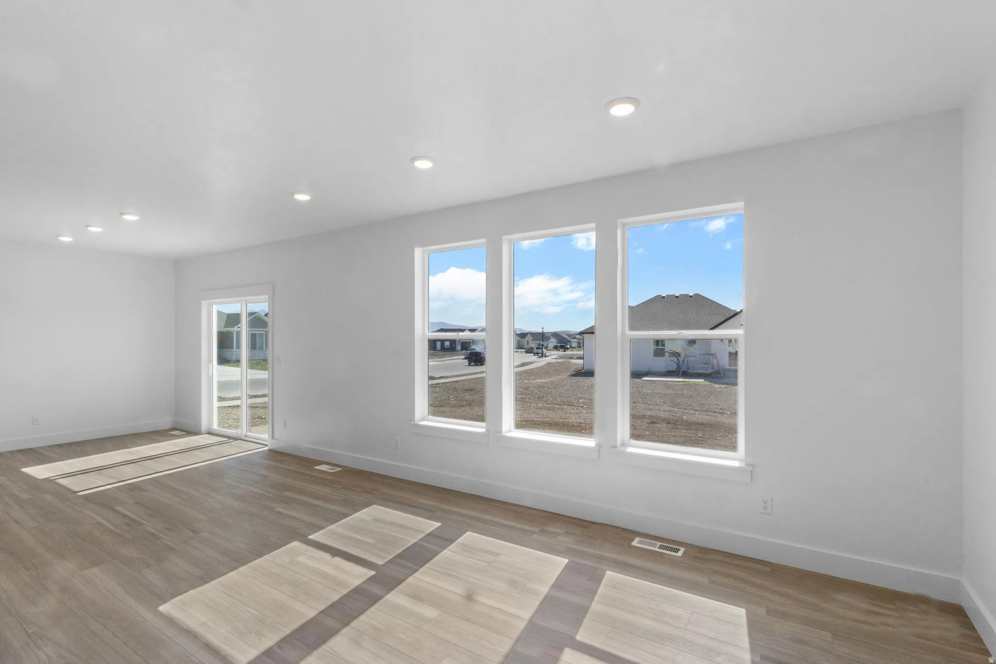 Spacious room featuring wood-finish flooring, recessed lighting, and multiple windows