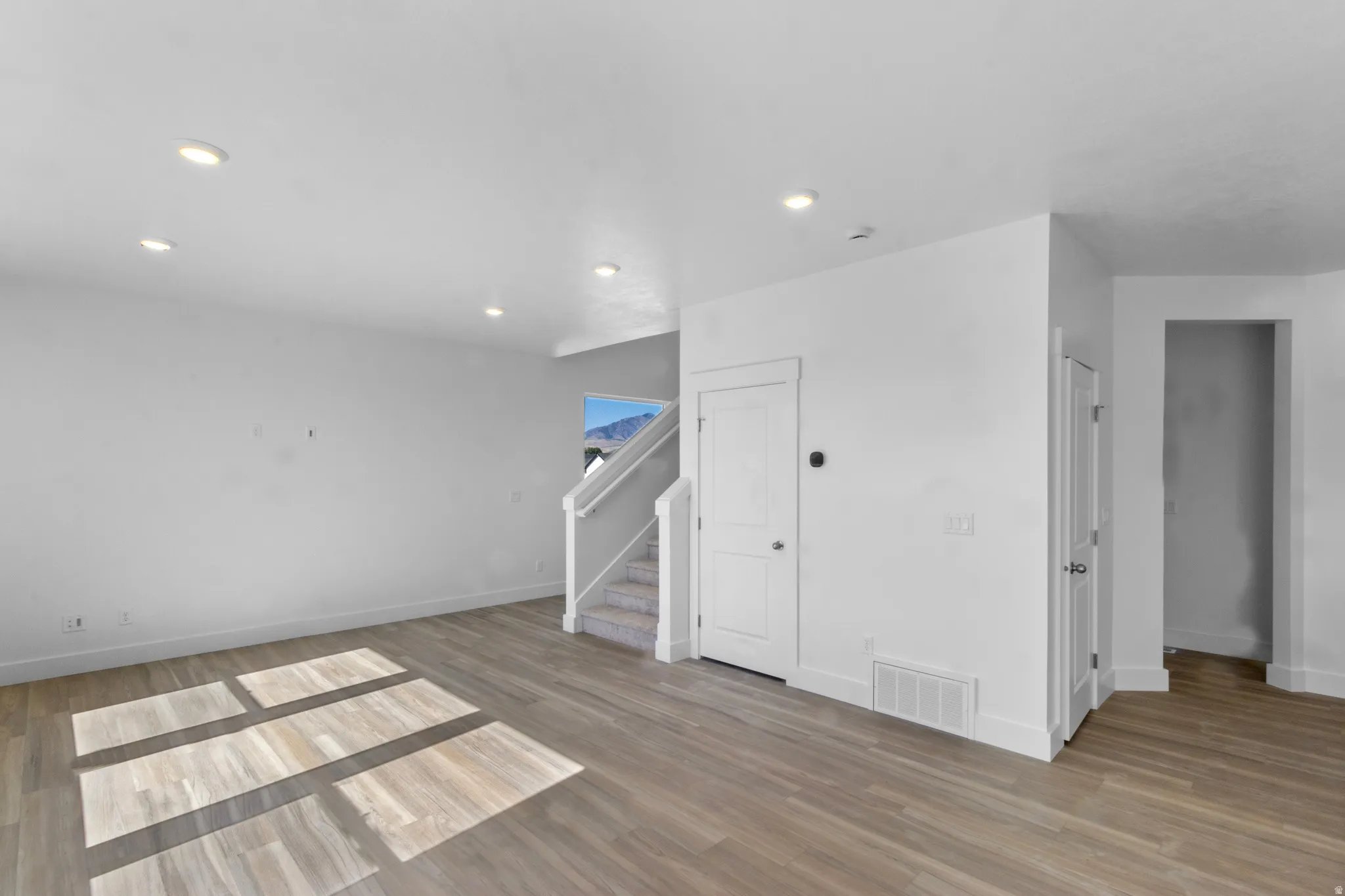 Spacious room featuring wood-finish flooring, recessed lighting, white walls, and a staircase with white risers and handrails