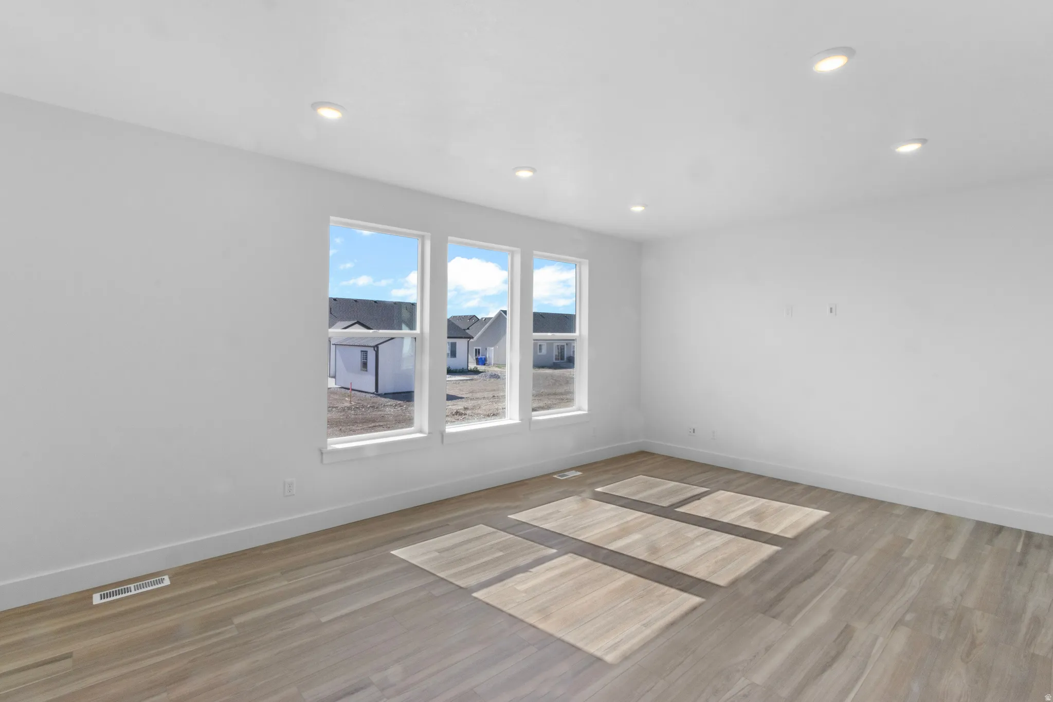 Spacious room featuring three large windows, recessed ceiling lighting, and wood-finish flooring