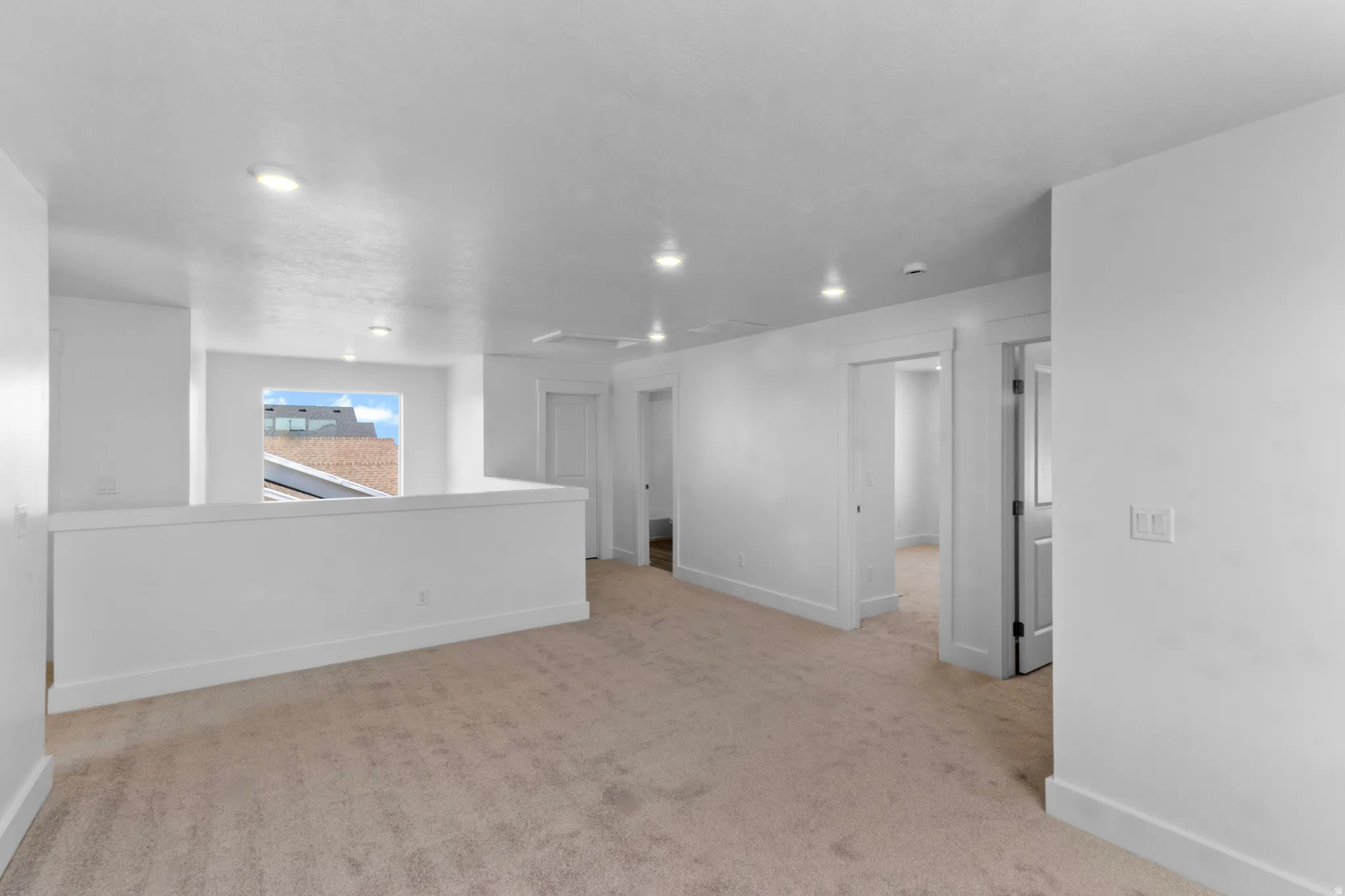 Open loft space featuring neutral carpeting, recessed lighting, white walls, white baseboards, and a half-wall partition