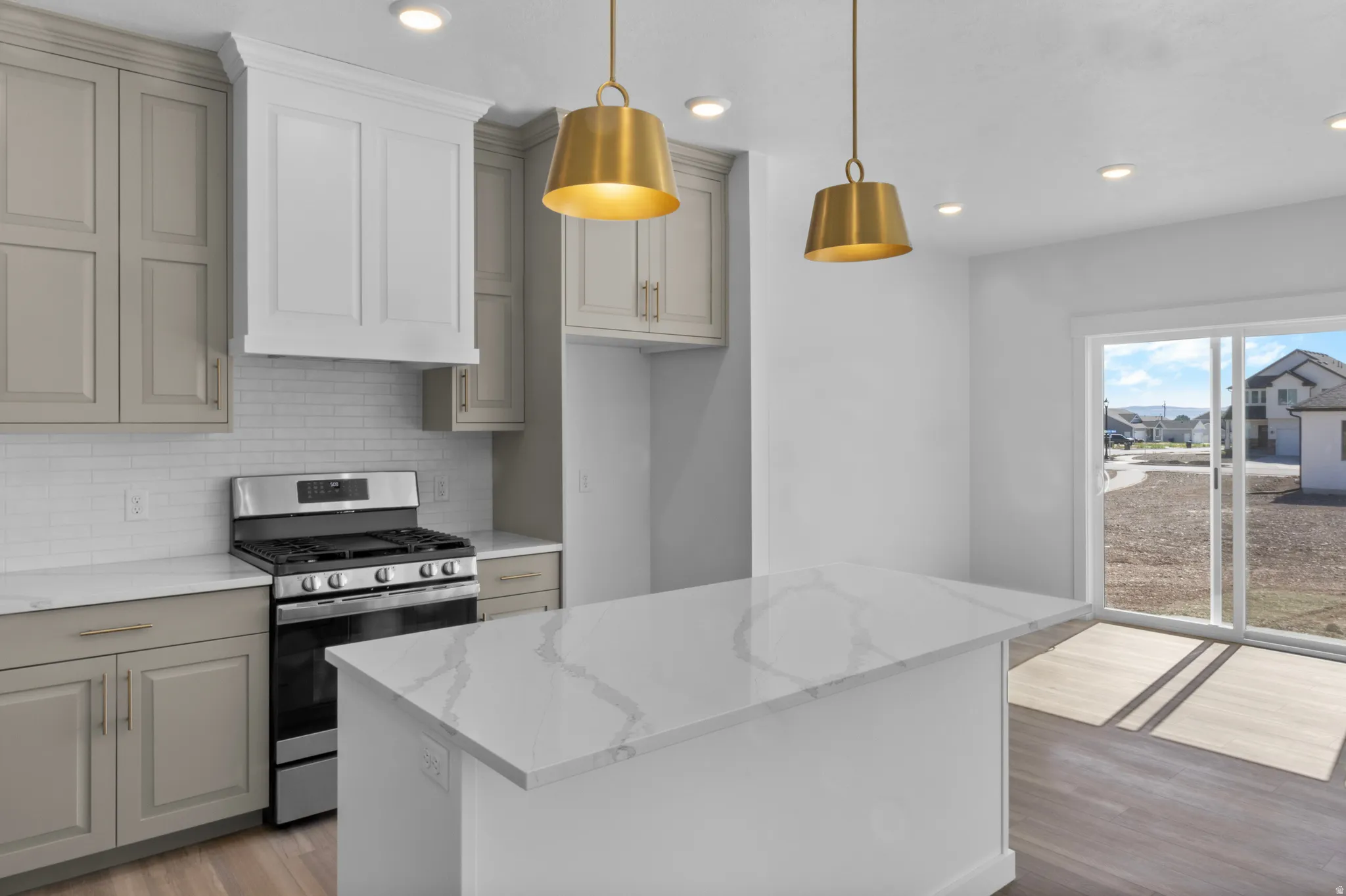 Kitchen featuring a large island with a patterned countertop, stainless steel range, white subway tile backsplash, and two-tone cabinetry with gold-toned hardware