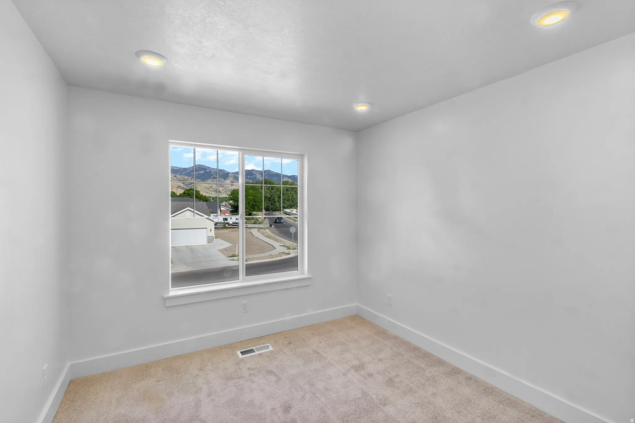 Recessed ceiling lighting illuminates a room with light-colored carpeting, white walls, and white baseboards
