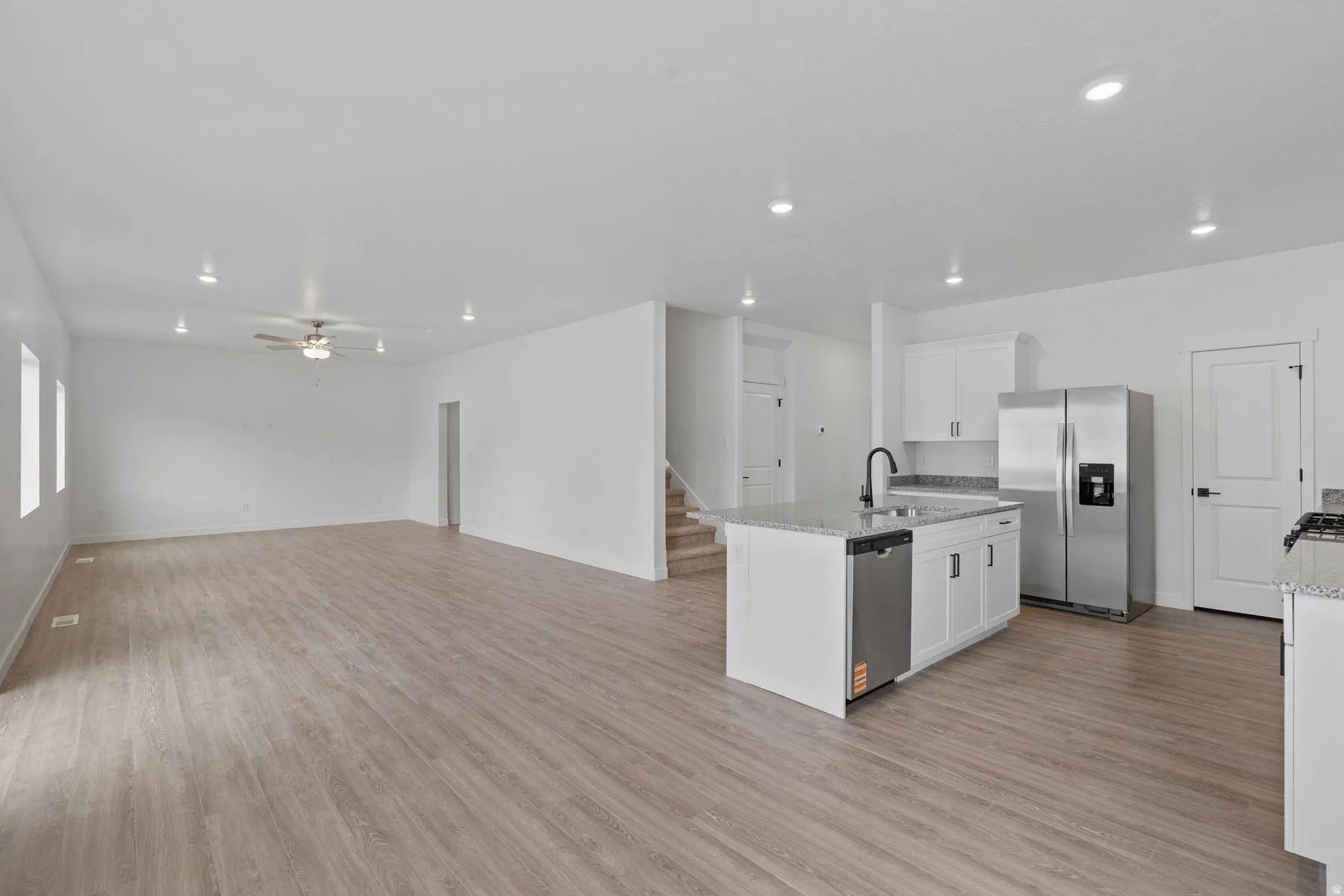 Contemporary kitchen featuring a center island with sink, stainless steel appliances, white cabinetry, and granite countertops