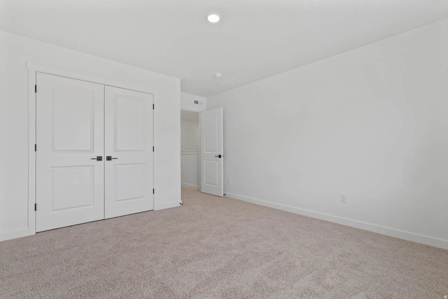 Neutral tone wall finish, plush carpet flooring, recessed ceiling light, white baseboards, and double closet doors with dark hardware