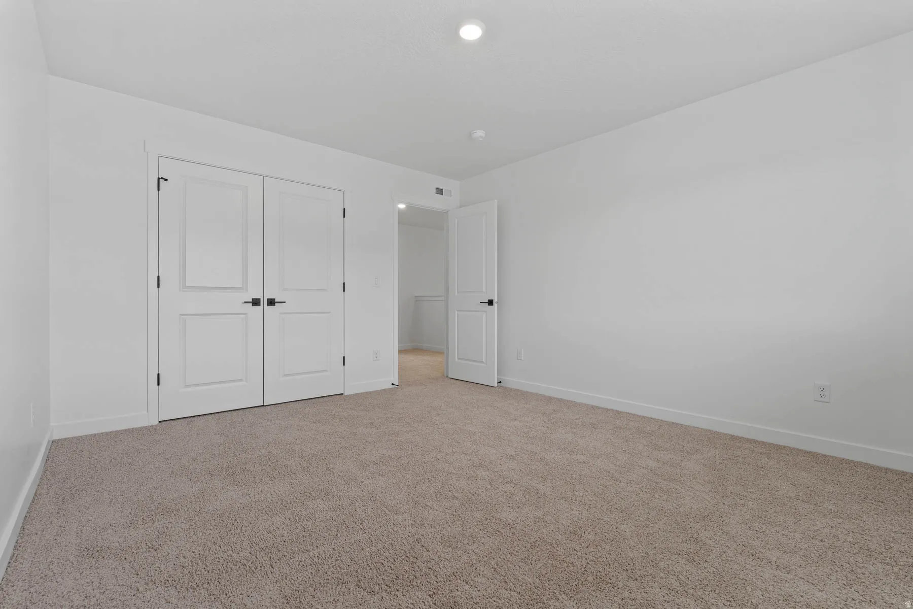 Neutral toned carpet flooring, white walls, white baseboards, and recessed lighting