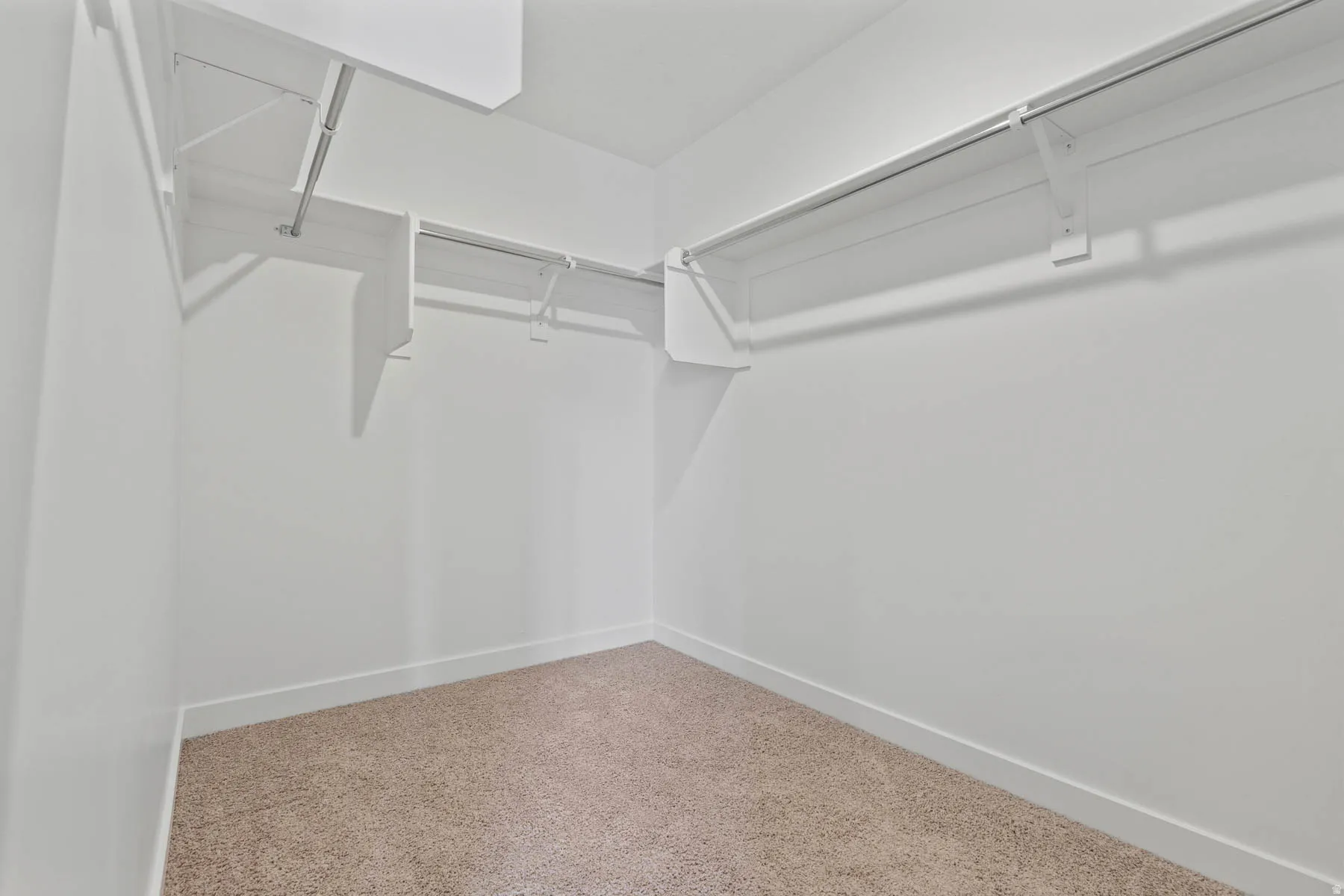 Walk-in closet featuring white wire shelving, metal hanging rods, light-colored carpet, white walls, and white baseboards