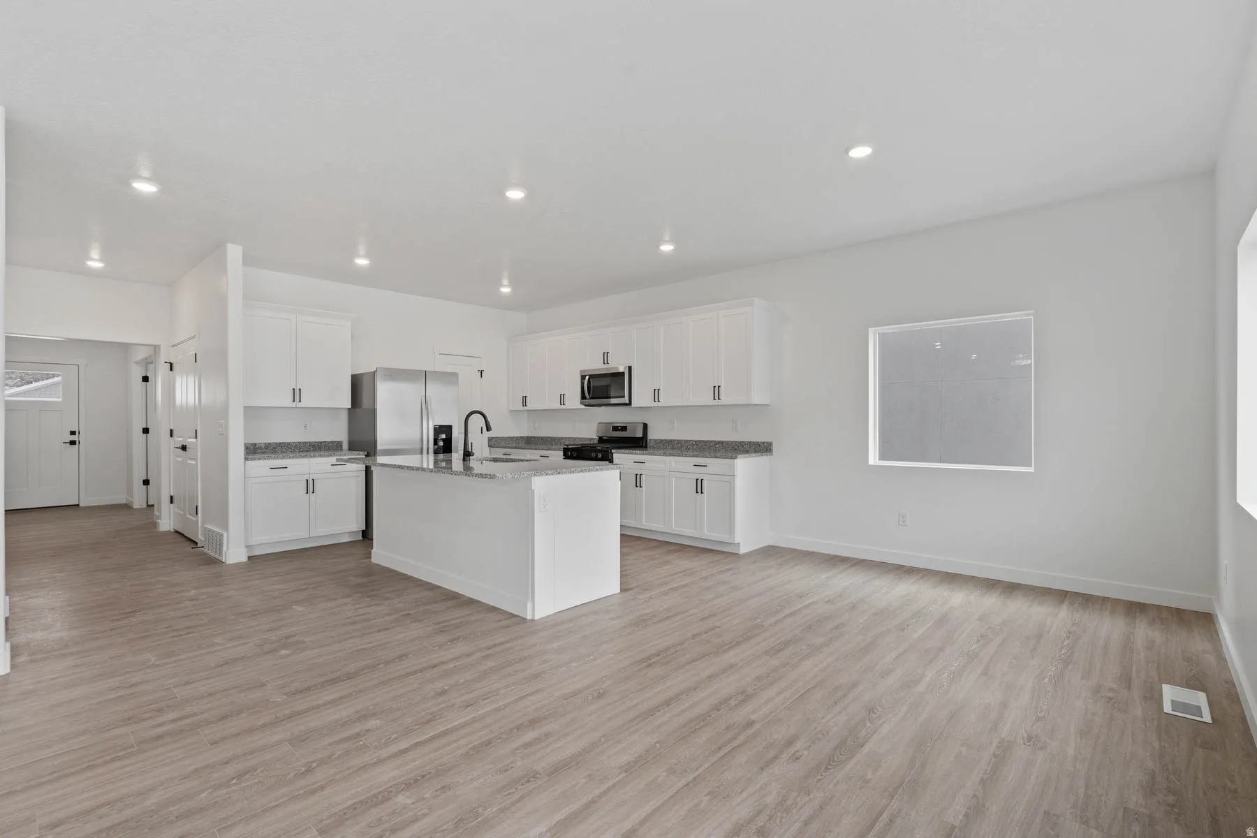 Open-concept living space featuring wood-finish flooring, recessed lighting, and a kitchen with white cabinetry